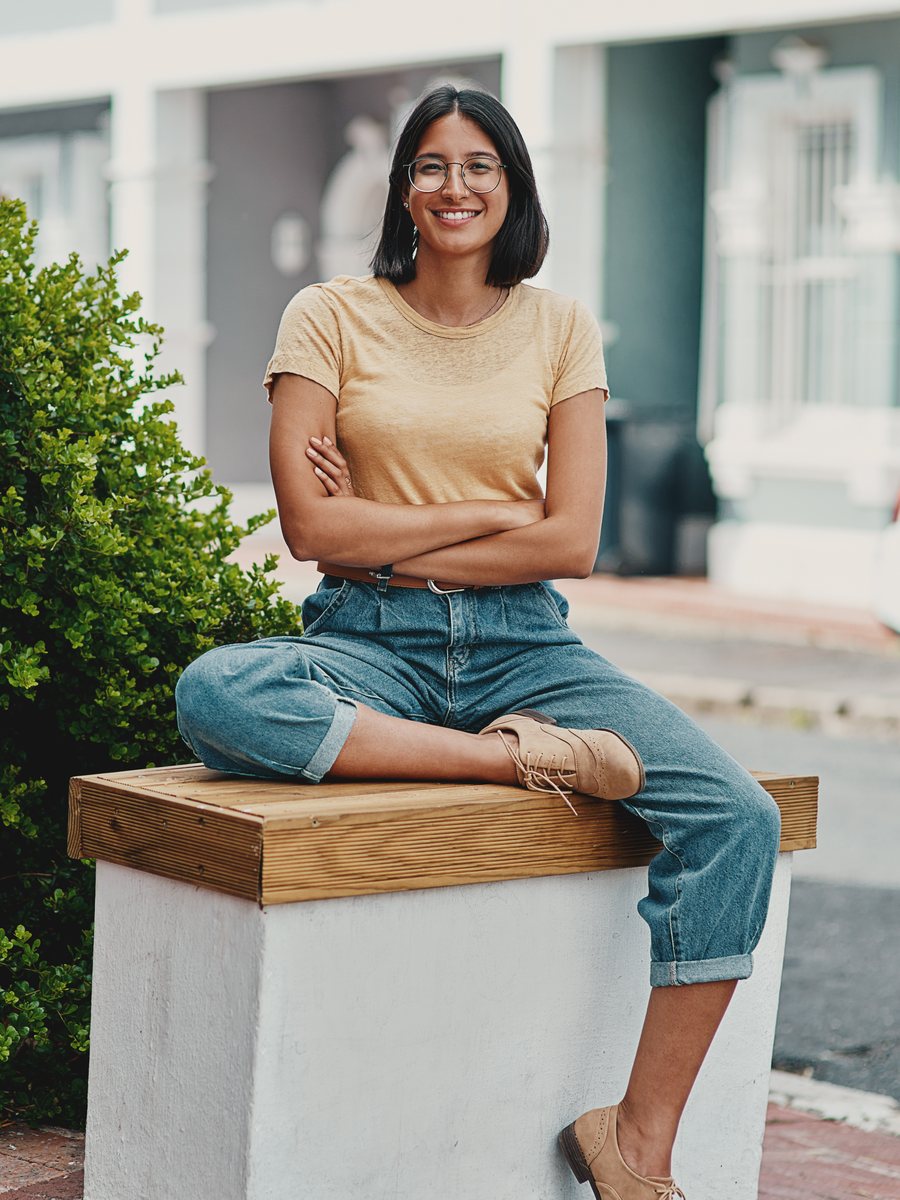 Priya S. sitting outside her home, arms crossed