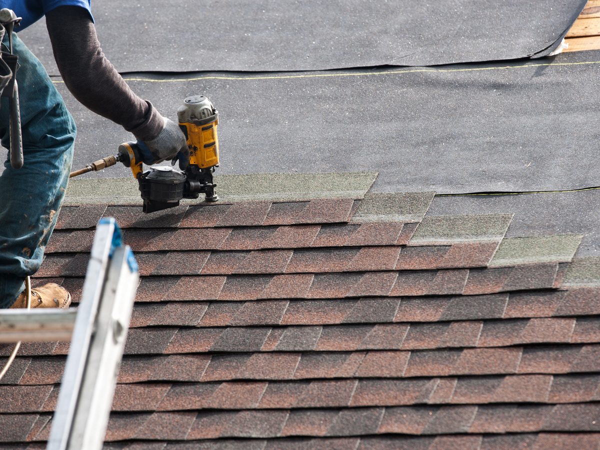 Roofer nailing new asphalt shingles on a residential roof