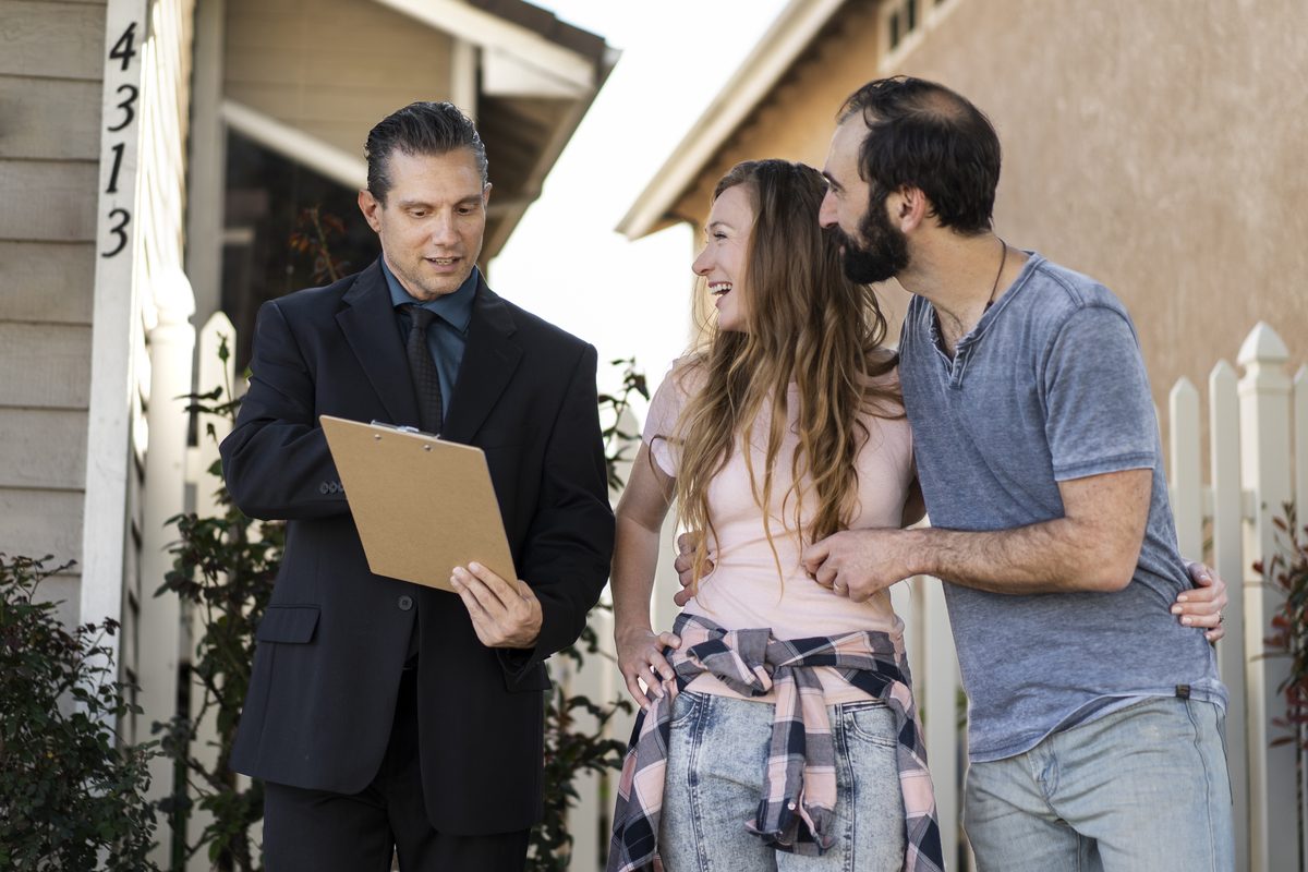 A project manager walks two homeowners through a written roof plan outside their house